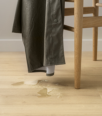 Jacke hängt über einem Stuhl, Wassertropfen fallen auf einen beigefarbenen Laminatfussboden